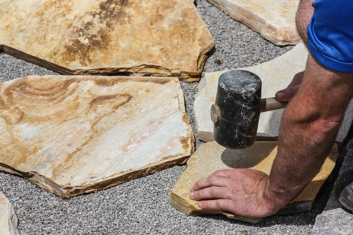 Person verlegt Steinplatte mit Gummihammer